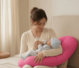 Mother holding her baby while seated with a pink Nurtura V-shaped support pillow providing cushioning.